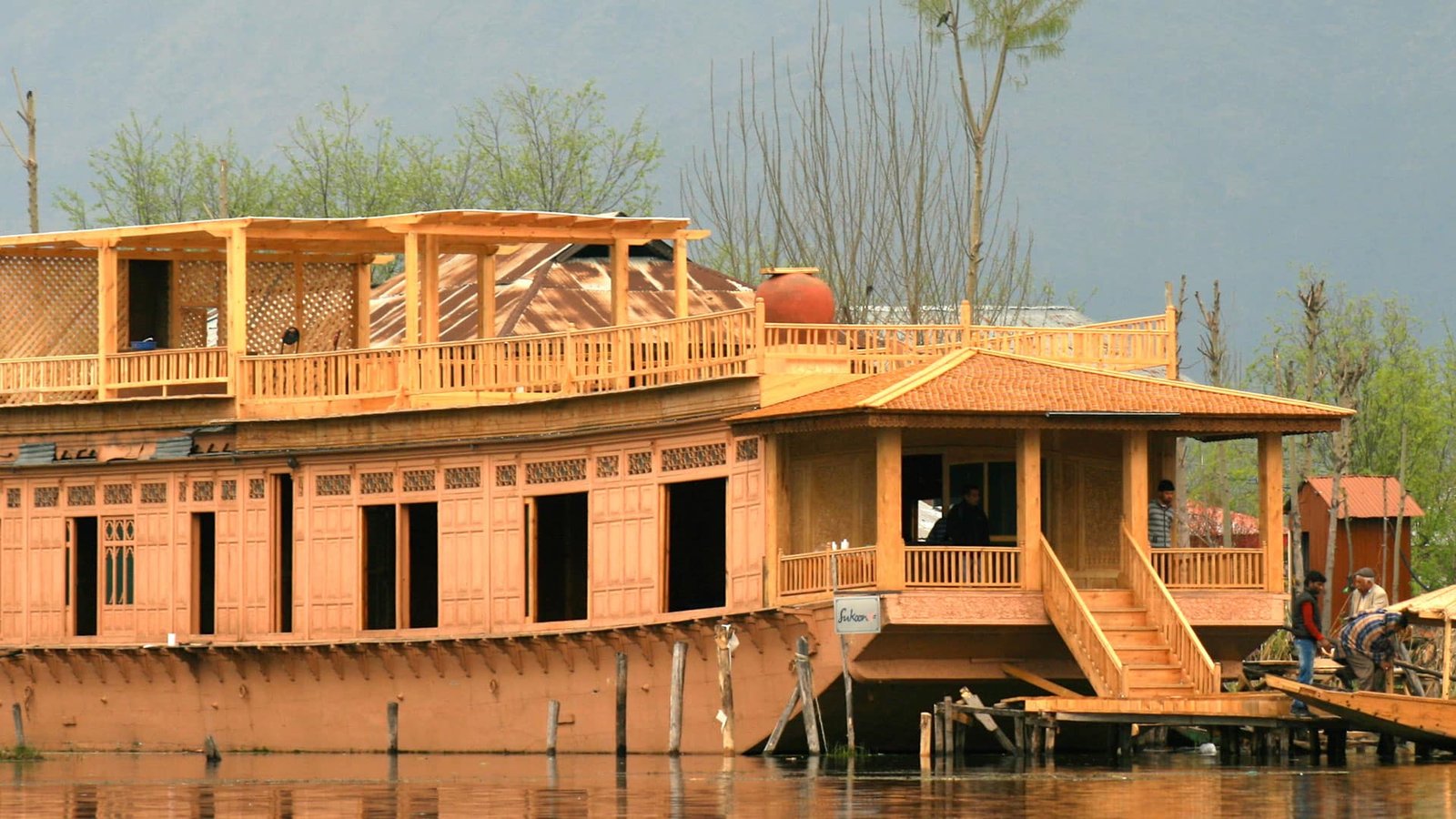 Wooden houseboat on Dal Lake in Srinagar with people and scenic mountain backdrop
