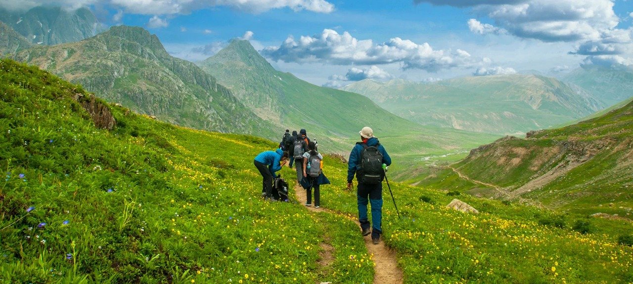 Group of trekkers walking through lush green meadows and scenic mountains during the Kashmir Great Lakes Trek