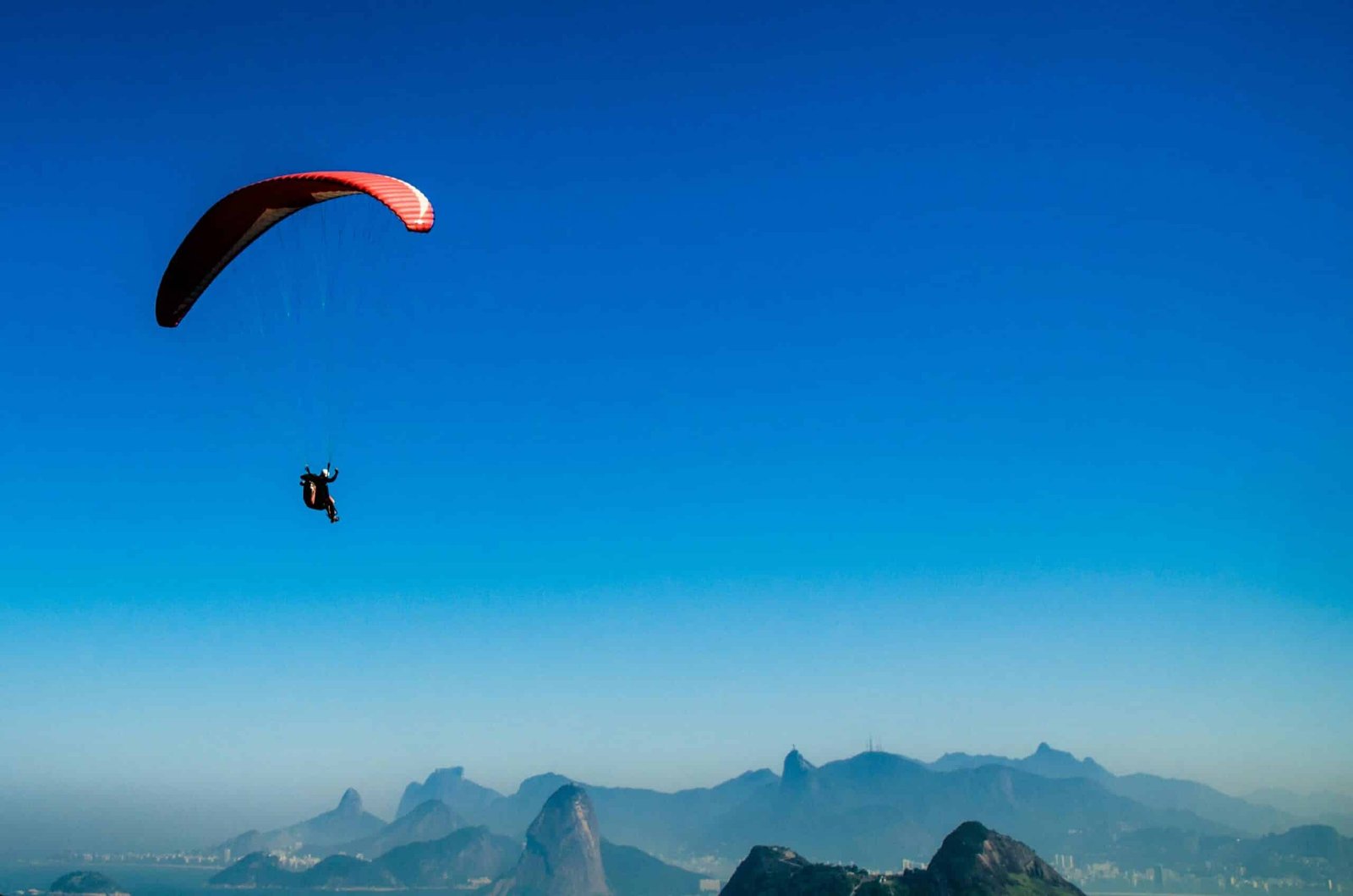 Paraglider flying high over Kashmir's mountains under a clear blue sky