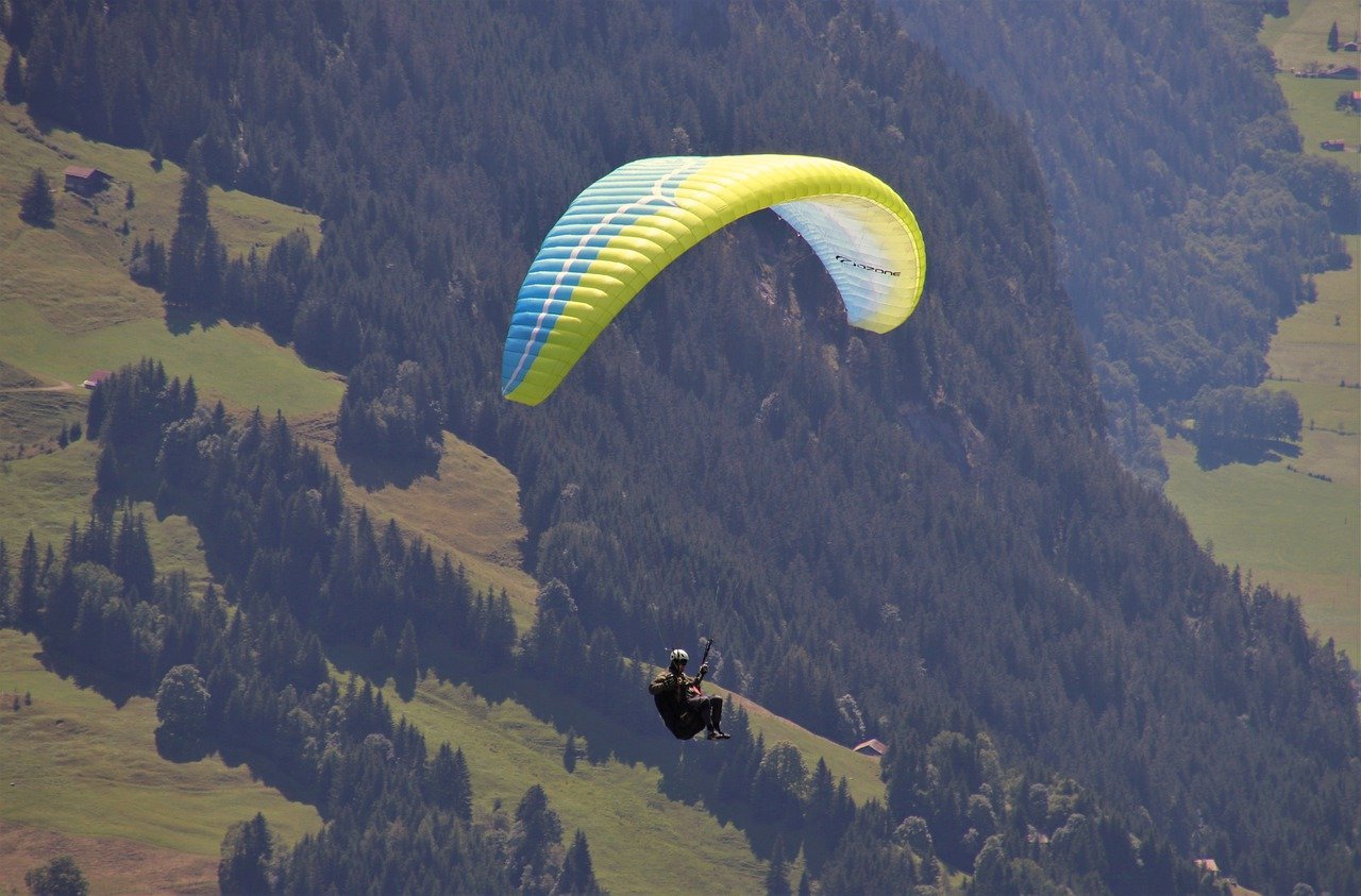 Person paragliding over green hills and forests.