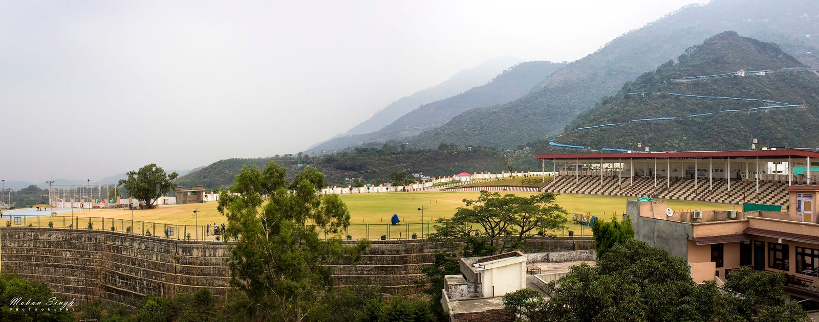 A sports stadium set in a valley with green hills and mountains in the background