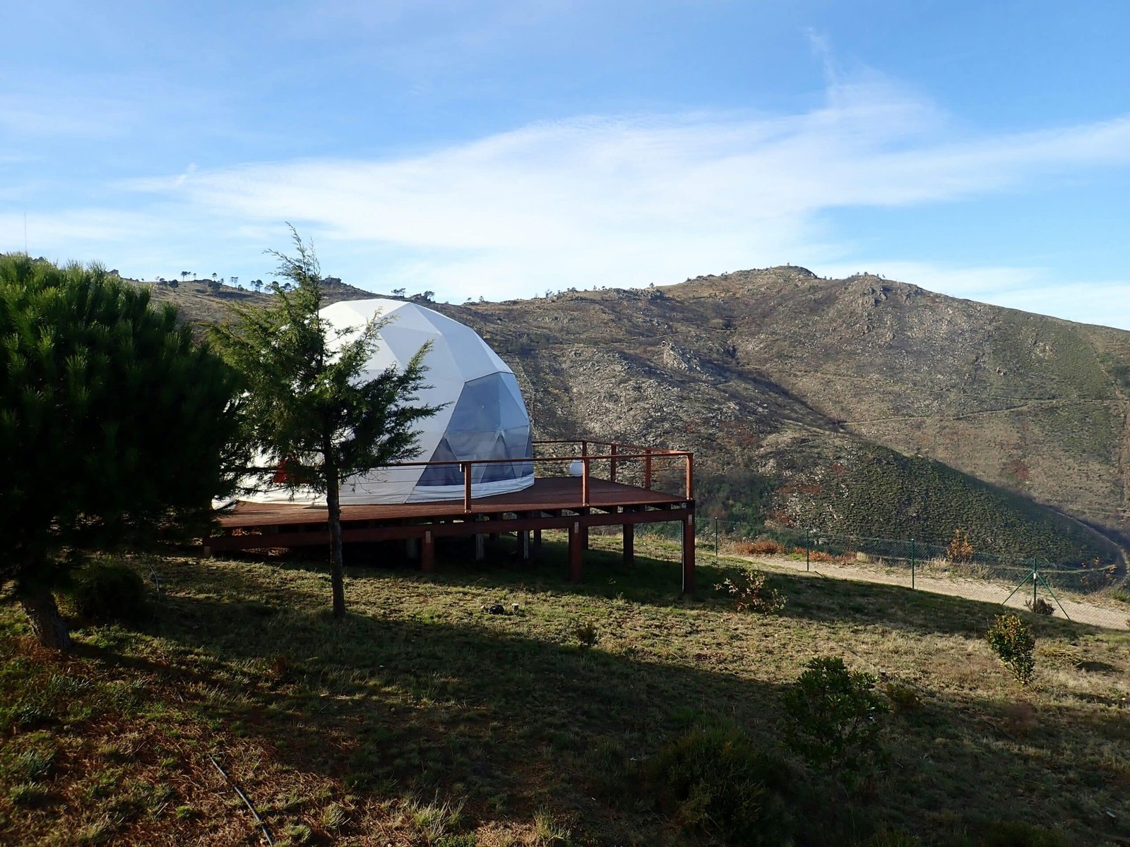 A dome-shaped tent set on a wooden deck, surrounded by hills and open skies in Srinagar