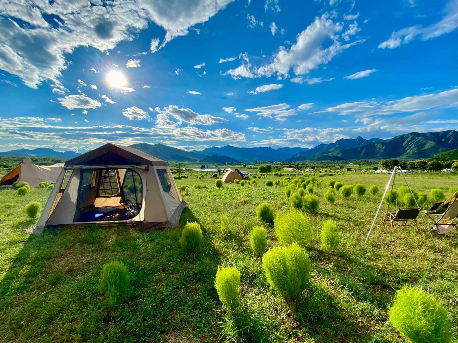 A cozy tent set up in a green field, with soft sunlight and mountains
