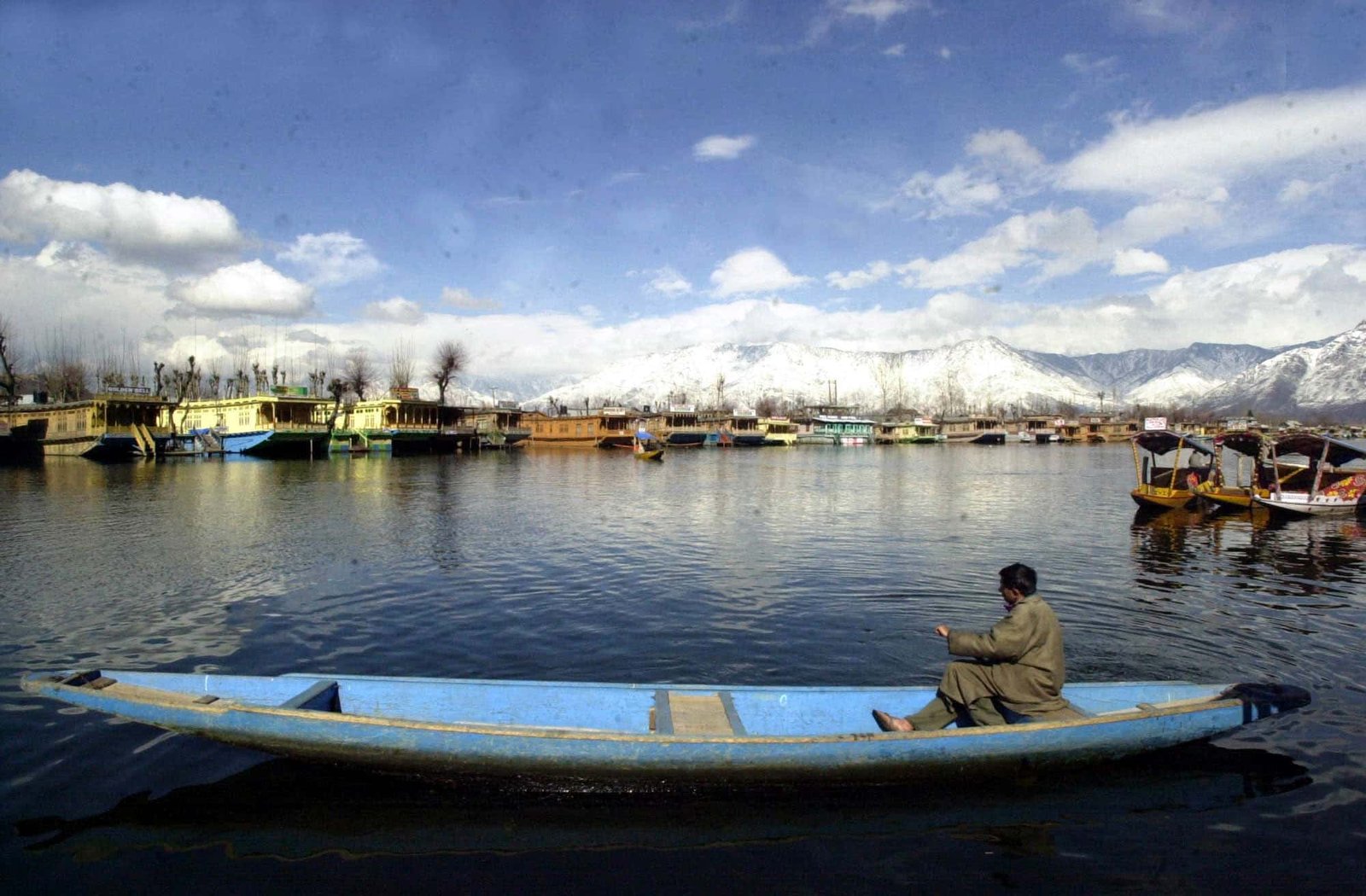 Man rowing a traditional boat on Dal Lake with houseboats