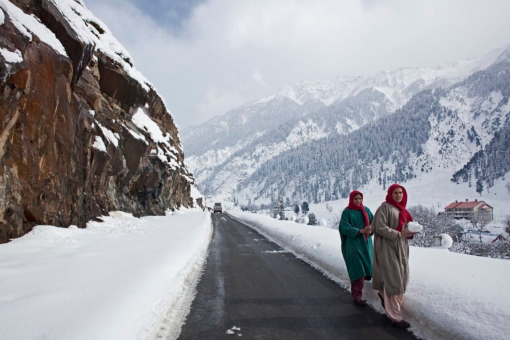 Two women walking on a snowy mountain road in Pahalgam during March