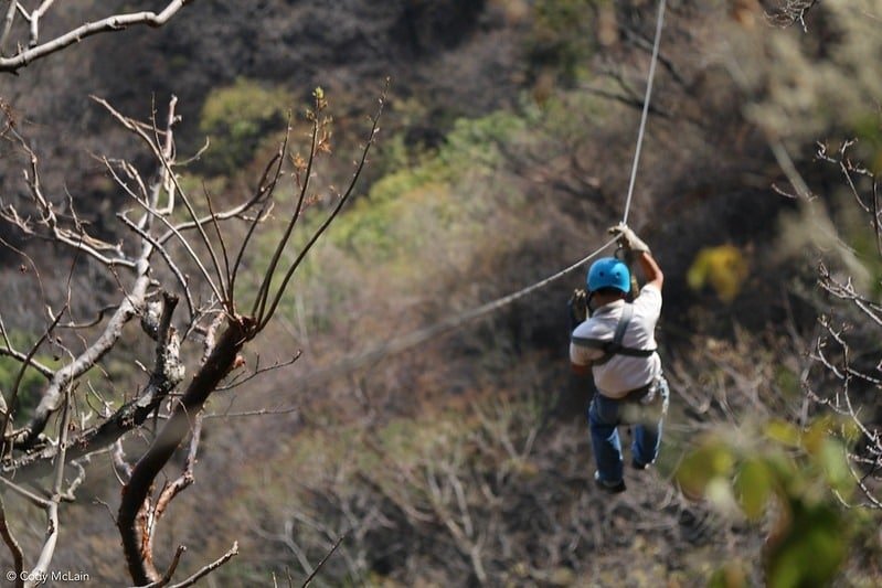 Person ziplining through the forested hills at Baisaran Valley, wearing a blue helmet and safety harness