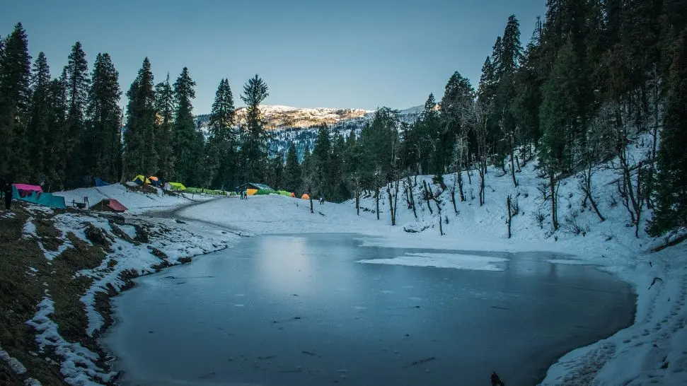 Snow-covered forest with a frozen lake and colorful tents in Manali