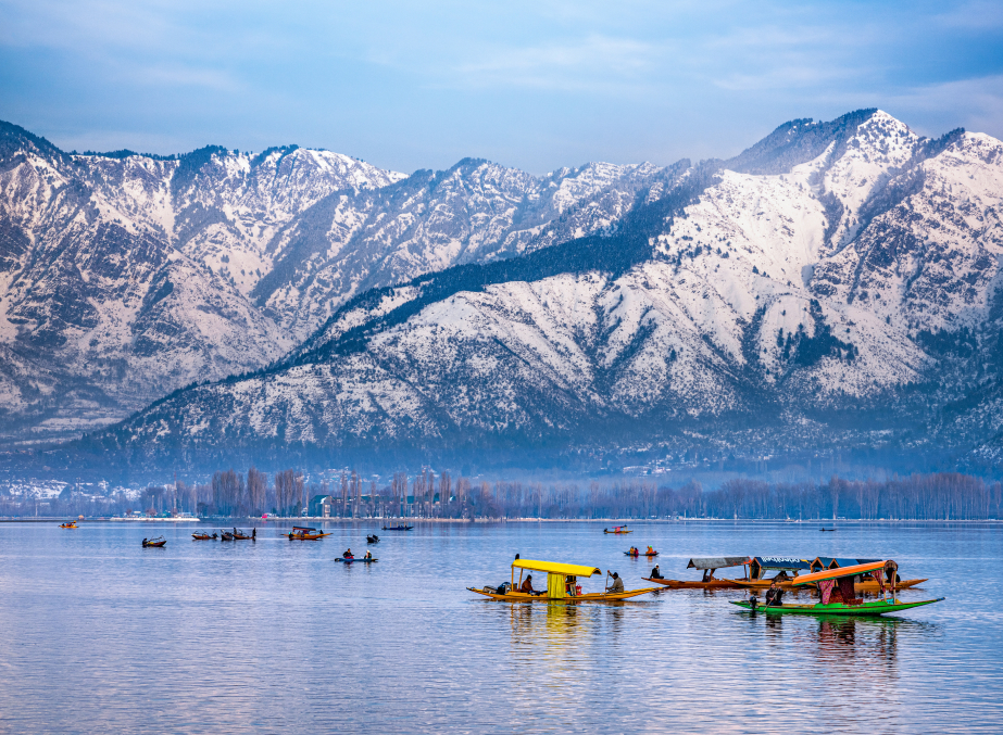 Shikaras floating on Dal Lake with snow-covered mountains in Kashmir