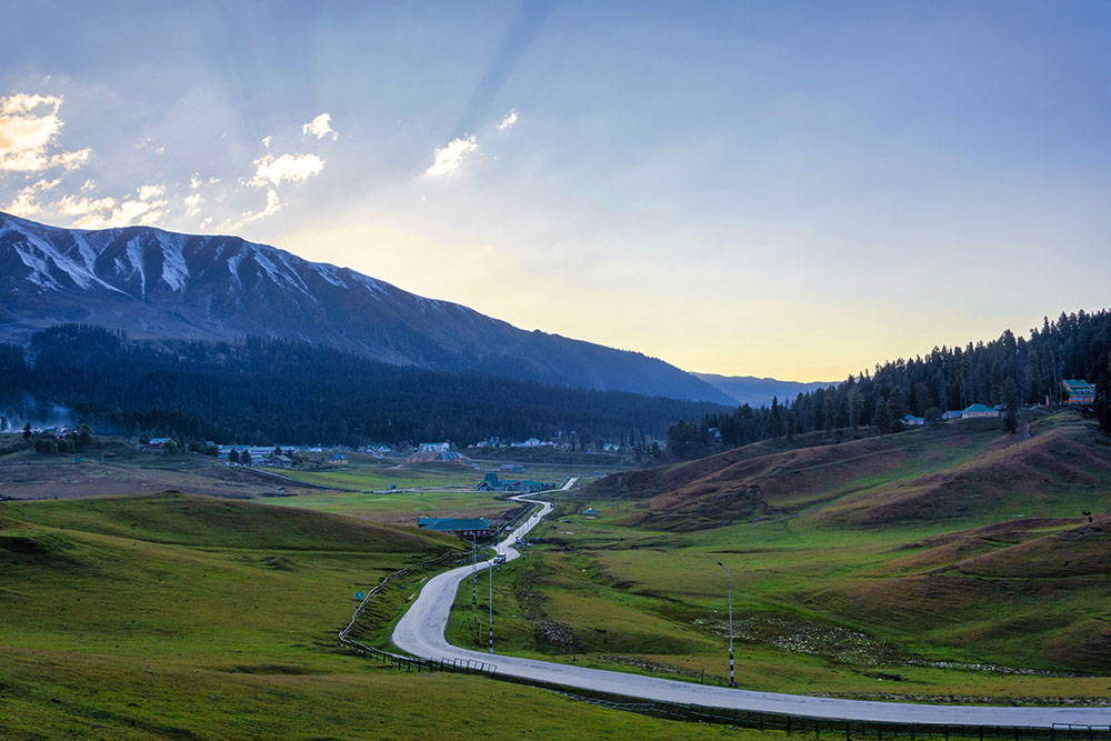 Scenic view of a winding road through lush green meadows and mountains near Srinagar at sunset