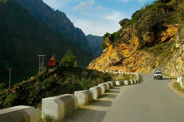 Scenic mountain road leading to Manali with a car and a small roadside temple