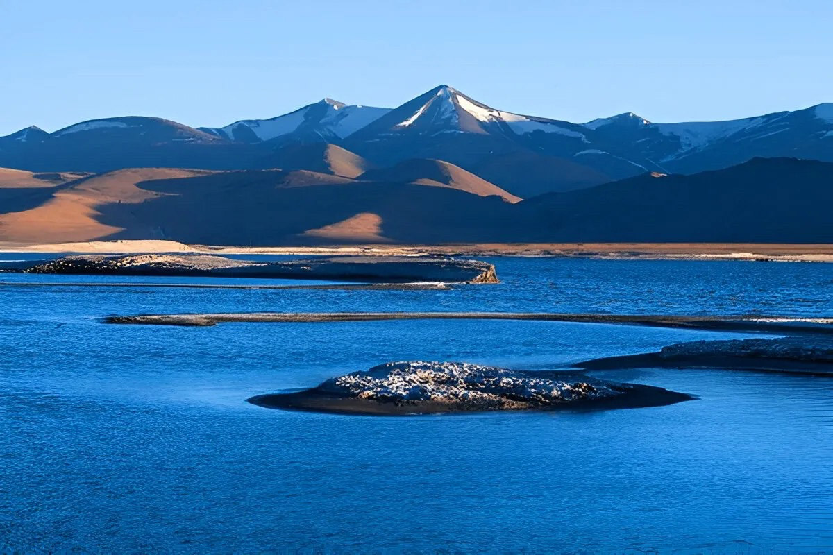 Tso Kar Lake with deep blue water, small islands, and snow-capped mountains in the background