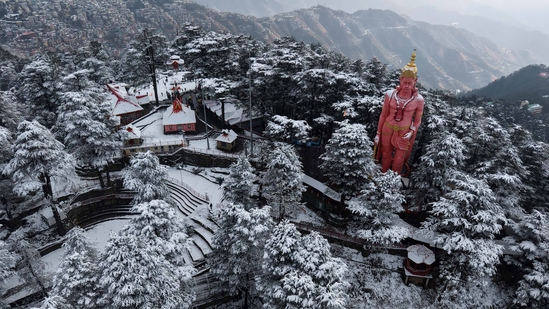 Snow-covered temple with large Hanuman statue in forested hills