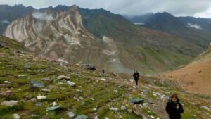 Trekkers walk up a rocky green trail with colorful mountains in the background, showing the beauty of Ladakh in July.
