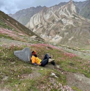 A trekker relaxes on a bed of wildflowers, surrounded by striking striped mountains, capturing the calm beauty of Ladakh in August.
